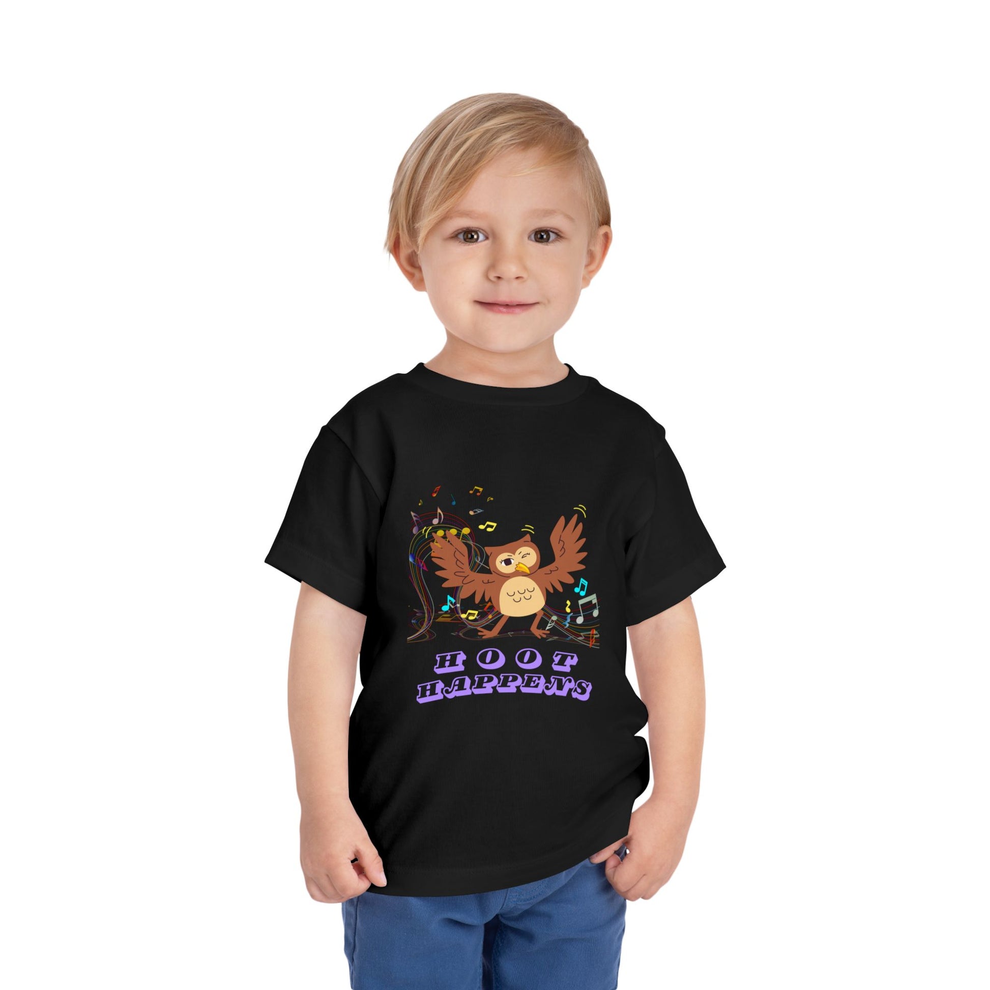 Child wearing a black toddler t-shirt with a colorful music notes and a dancing owl, 'Hoot happens' text 