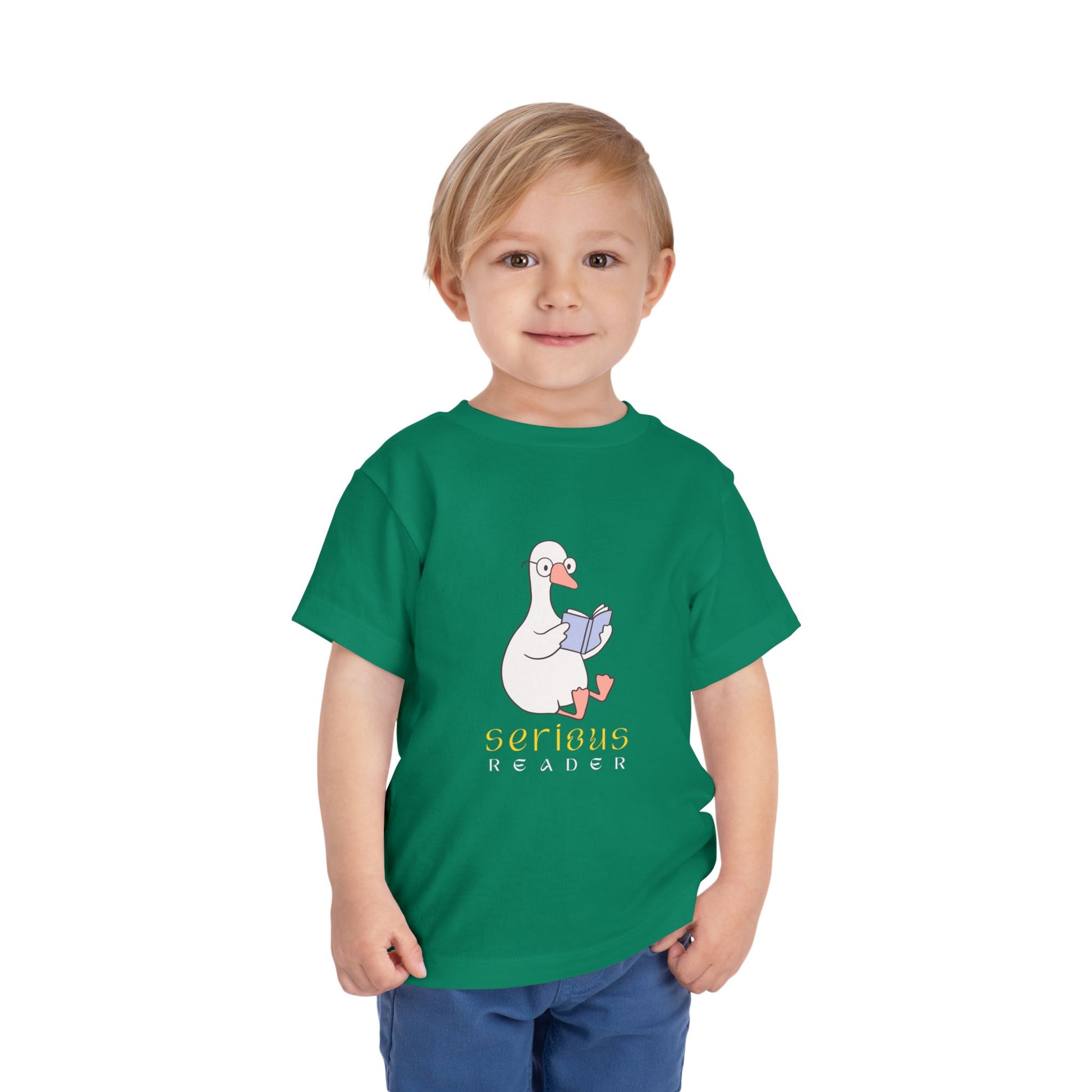 Toddler wearing a green t-shirt with a cartoon duck or goose reading a book and 'Serious Reader' text 