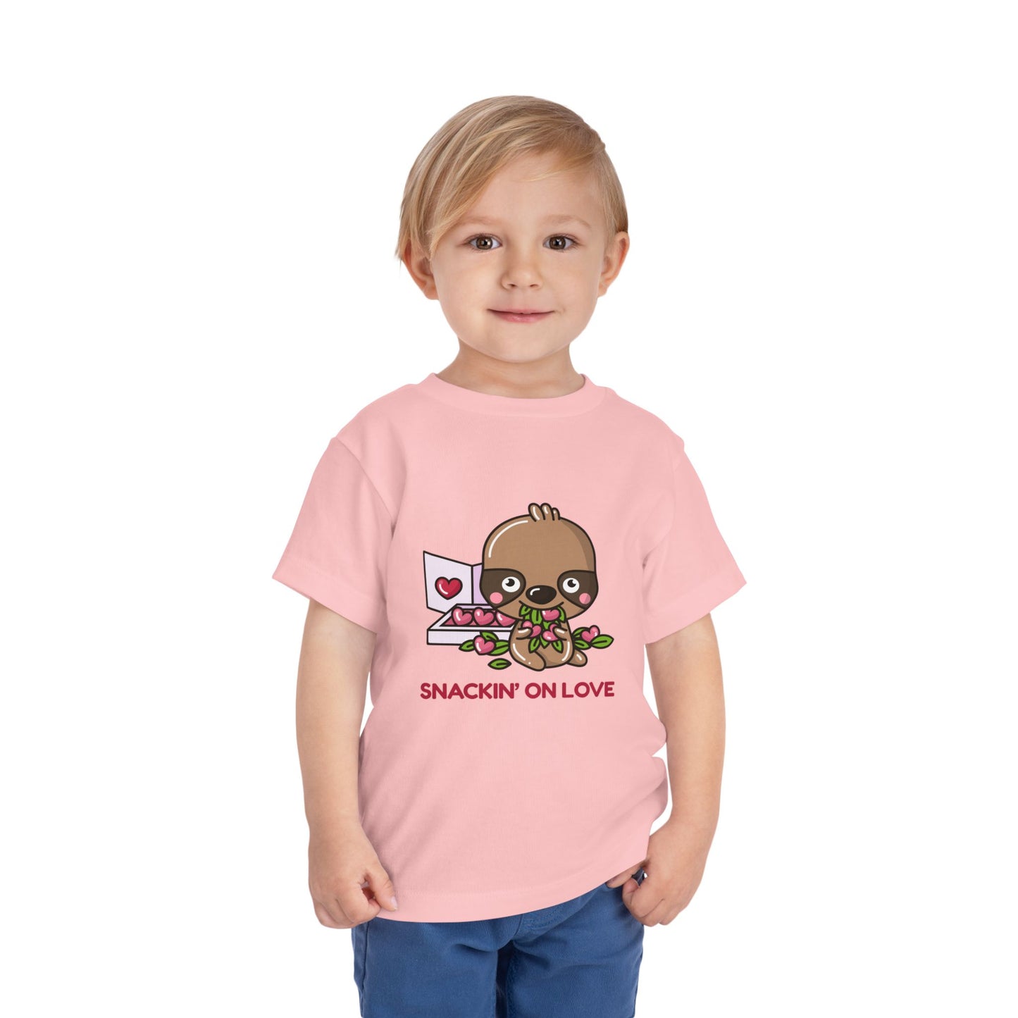 Child wearing a pink toddler t-shirt with a cartoon eating a box of heart shaped candies, text 'SNACKIN' ON LOVE'
