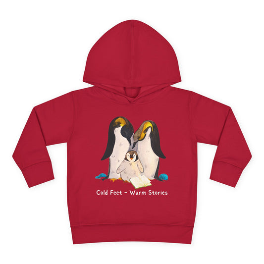 Cartoon penguin family huddled together reading an open book with the words “Cold Feet • Warm Stories” above — printed on a cozy toddler hoodie.