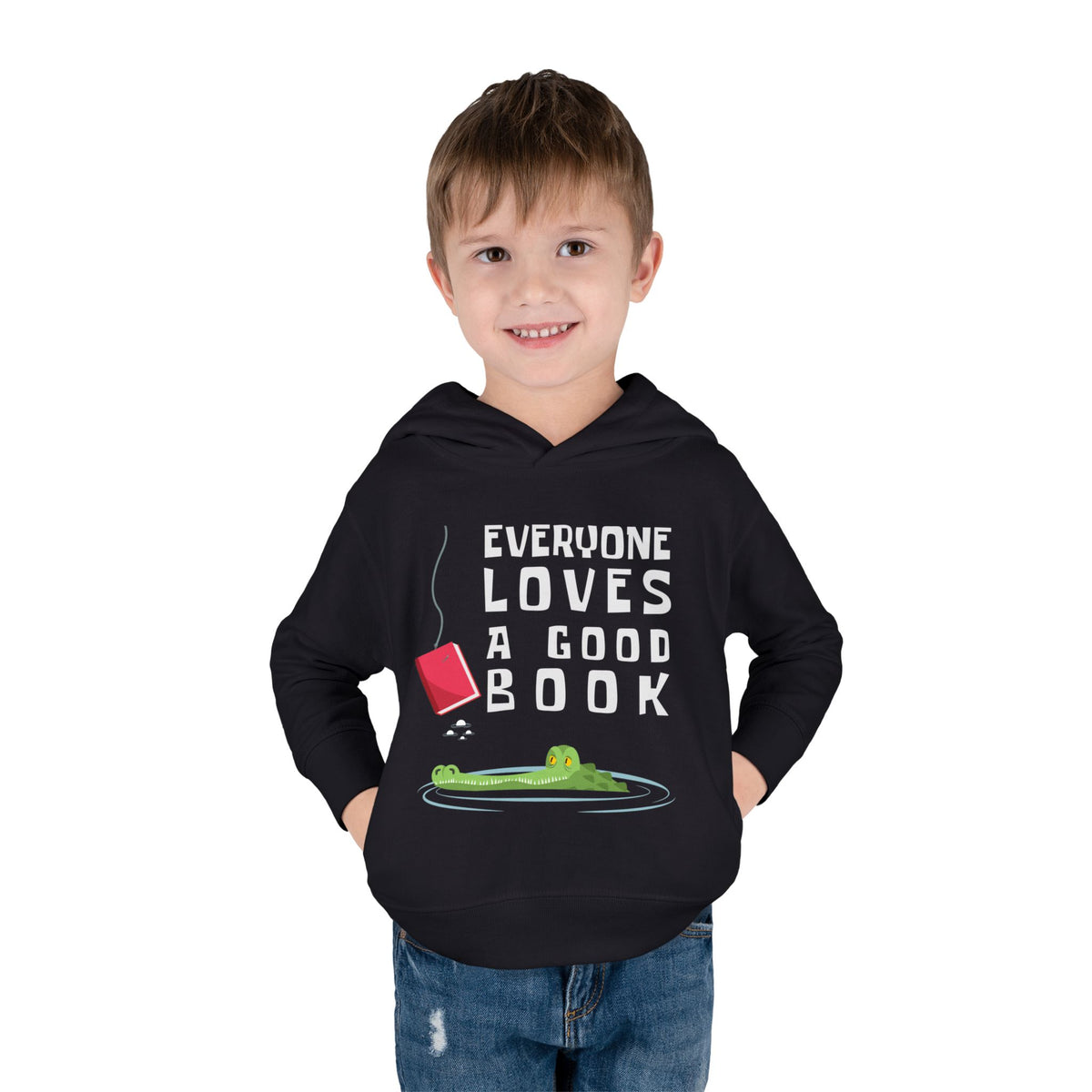 Little boy wearing a black  toddler pullover hoodie with a graphic print on the front. The print features the text 'EVERYONE LOVES A GOOD BOOK' in white capital letters, accompanied by an illustration of a green alligator in a pool of water with a red book hanging above it, on a solid white background.