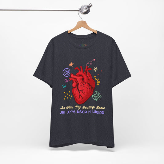 Dark gray t-shirt with a red anatomical heart surrounded by colorful doodles and text "Be Still My Beathing Heart. JK! Let's Keep It Weird'