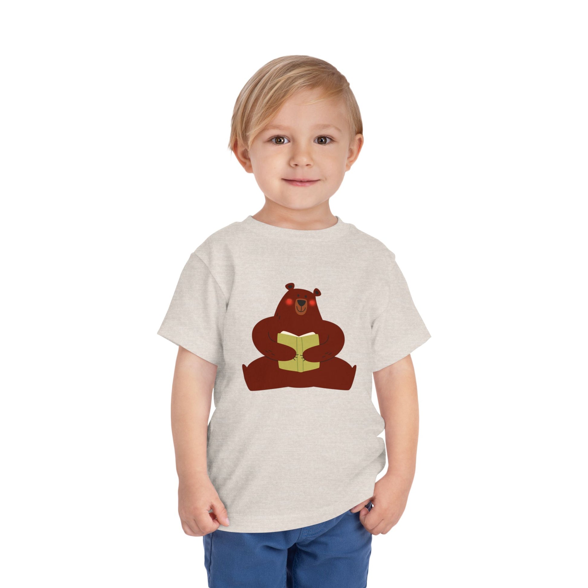 Toddler wearing a sandy beige t-shirt with a blushing sear holding a book