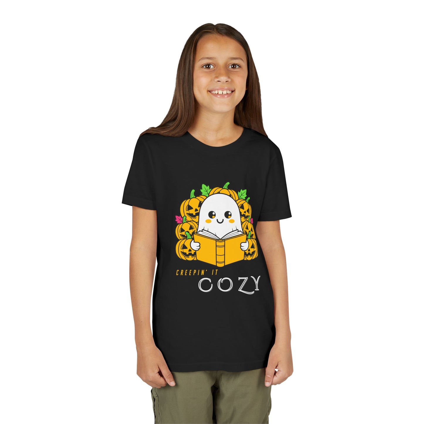 Girl wearing a black t-shirt with a ghost reading a book in a pumpkin patch with text 'Creepin' It Cozy'