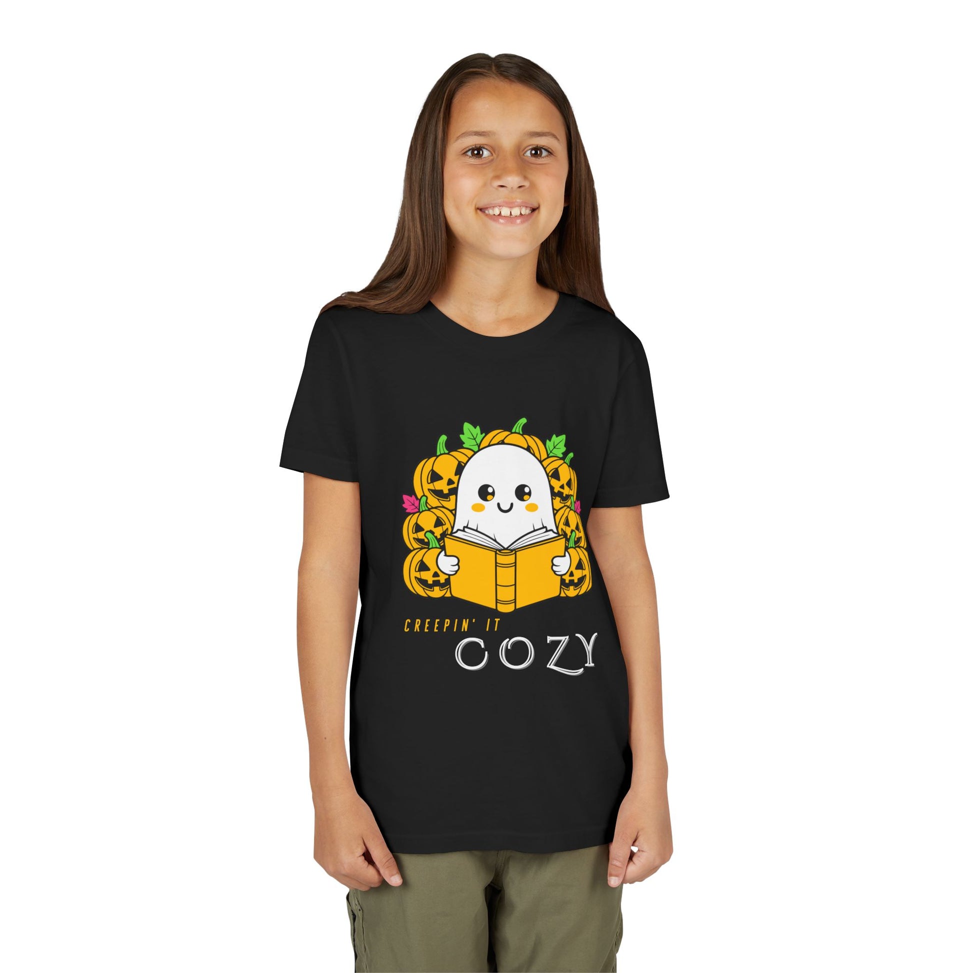 Girl wearing a black t-shirt with a ghost reading a book in a pumpkin patch with text 'Creepin' It Cozy'