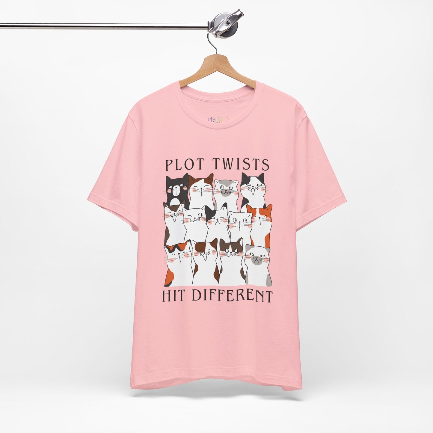 Pink t-shirt with rows of cats making different faces and text 'Plot Twists Hit Different' 