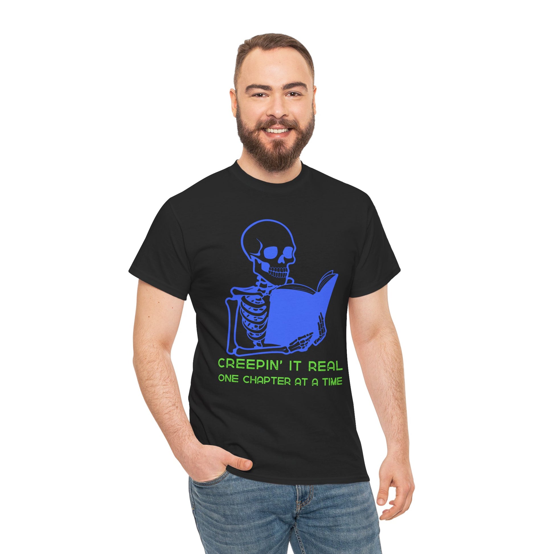 Man wearing a black t-shirt with blue skeleton graphic reading a book and green text 'Creepin' It Real One Chapter At A Time' on a hanger against a white background