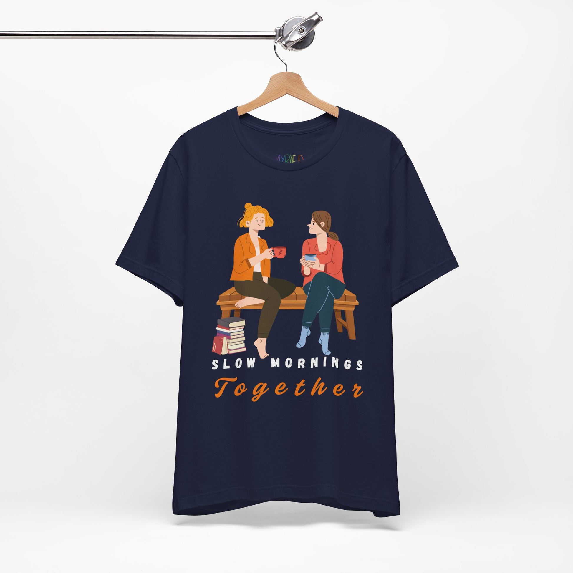 Navy blue t-shirt with graphic of two people sitting on a bench together, hot beverages in their hands, book at their feet and 'Slow Mornings Together' text below the image