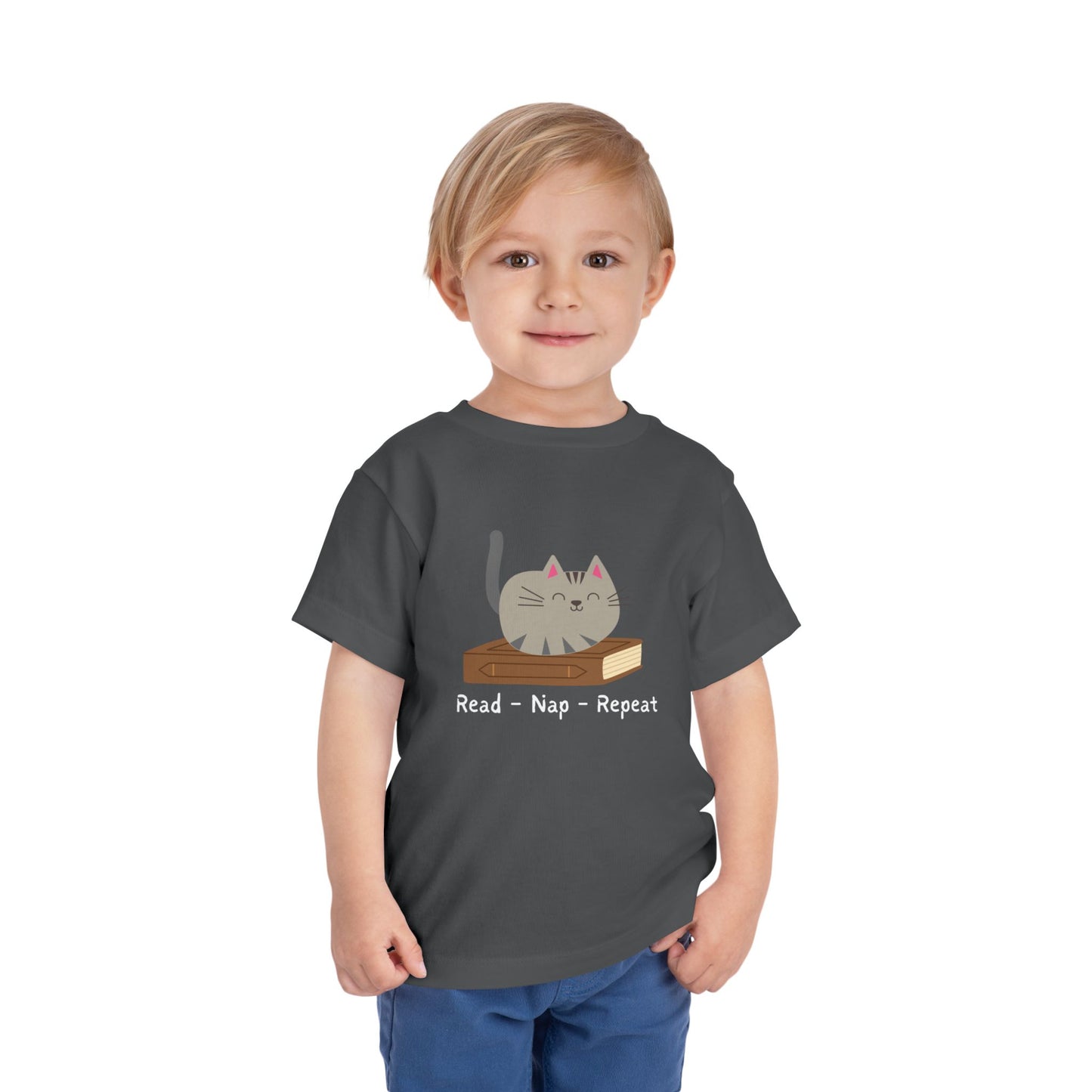Toddler wearing a gray t-shirt with a cat sitting on a book with text 'Read - Nap - Repeat' 