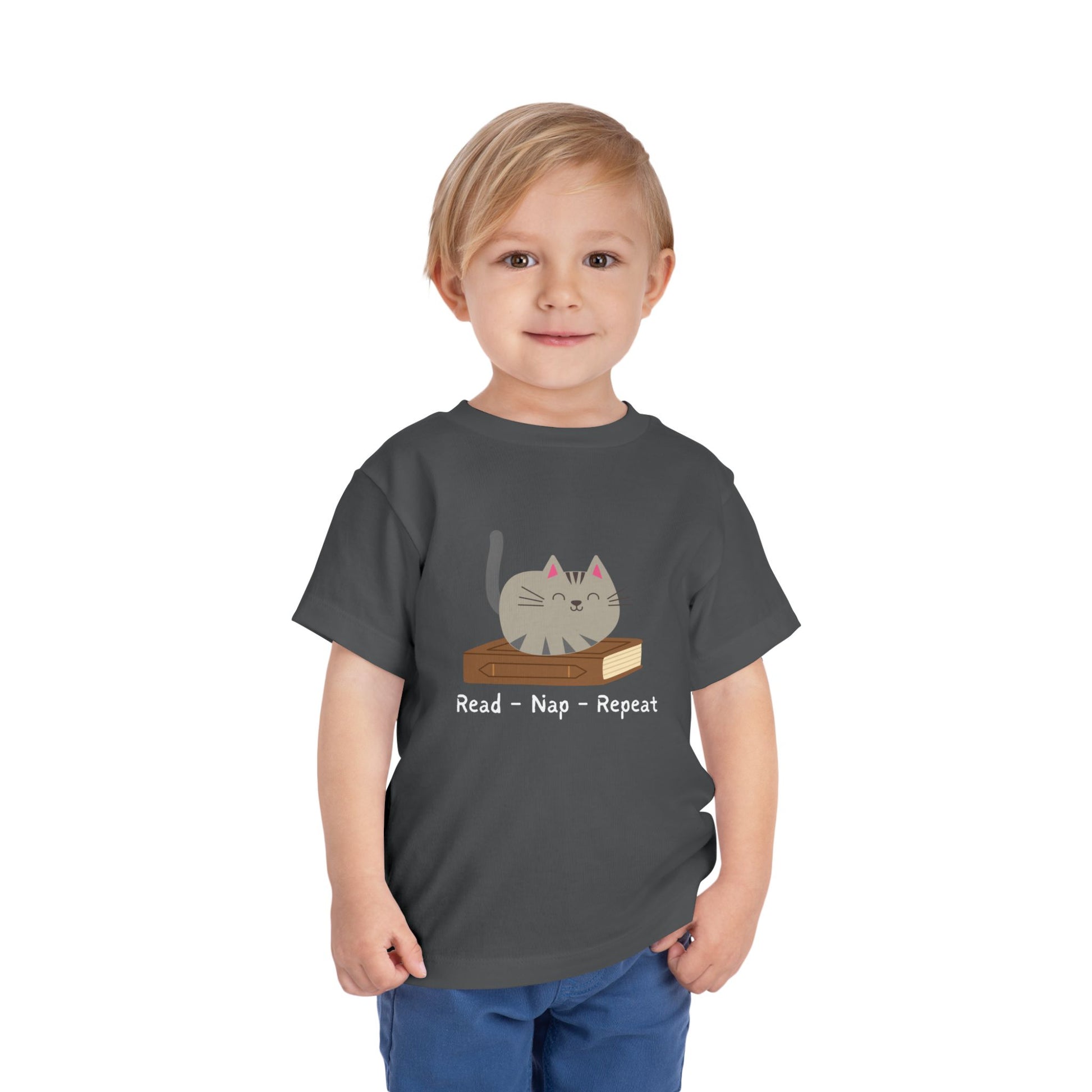 Toddler wearing a gray t-shirt with a cat sitting on a book with text 'Read - Nap - Repeat' 