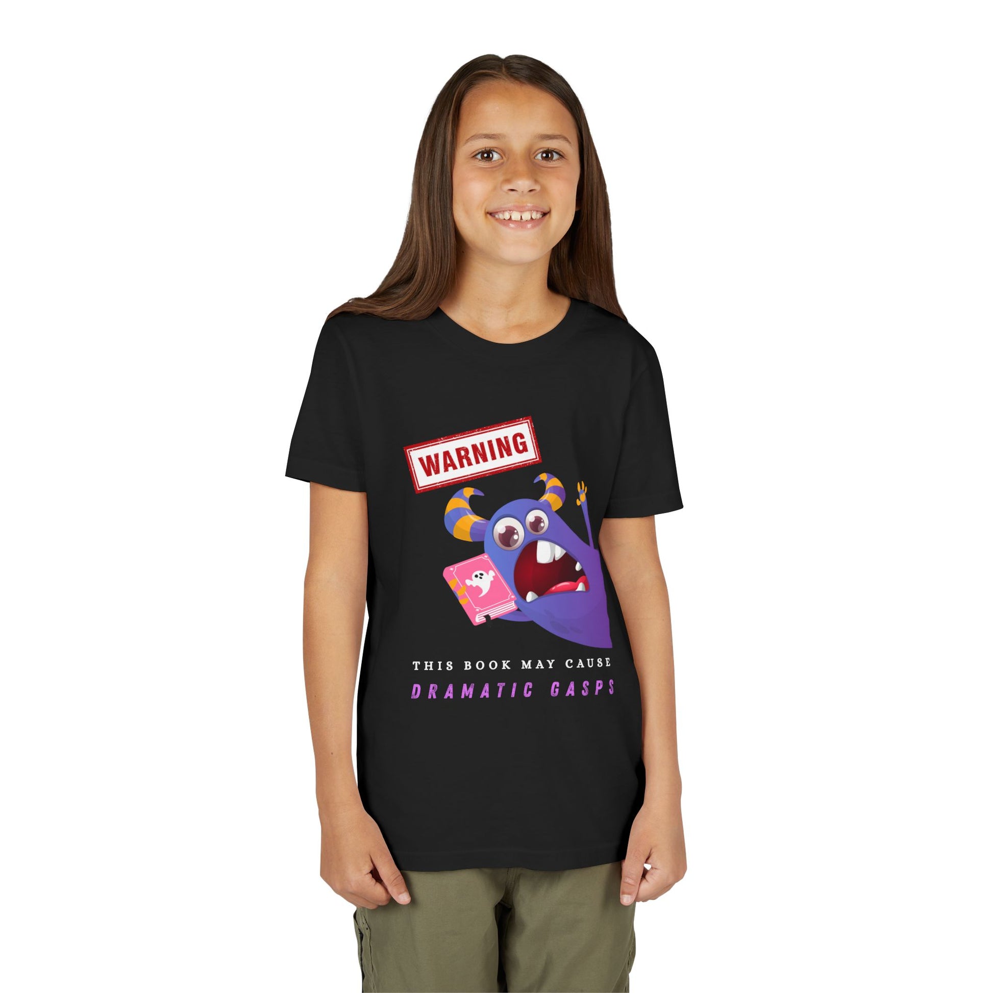 Girl wearing a black t-shirt with a purple monster urgently leaning in with a ghost book, a WARNING sign overhead, and text below 'This Book May Cause Dramatic Gasps'