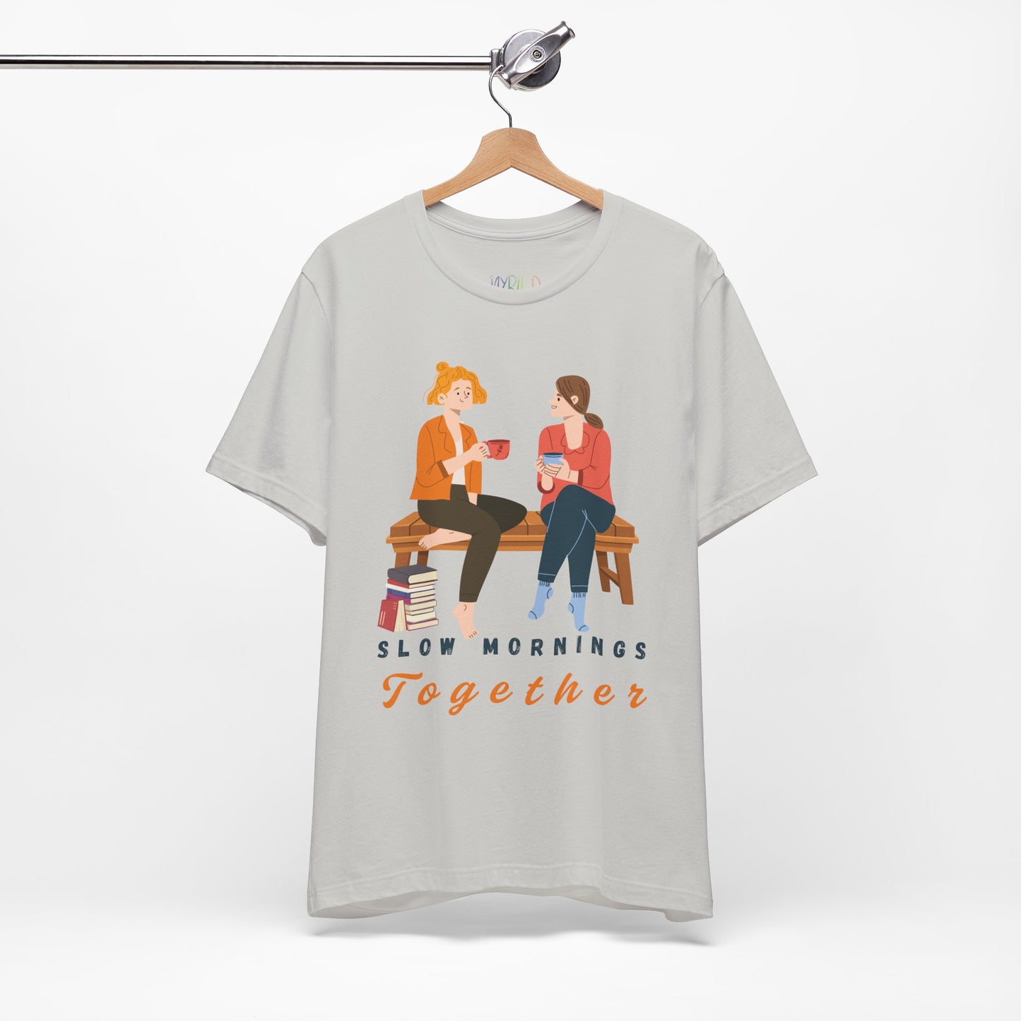 Gray t-shirt with graphic of two people sitting on a bench together, hot beverages in their hands, book at their feet and 'Slow Mornings Together' text below the image