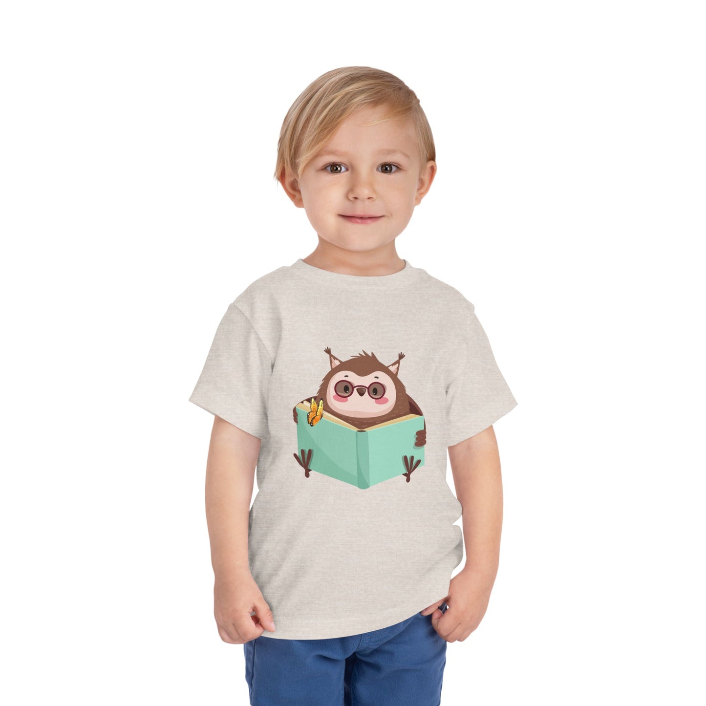 Child wearing a beige toddler t-shirt with a cartoon own reading a book with a butterfly perched on top