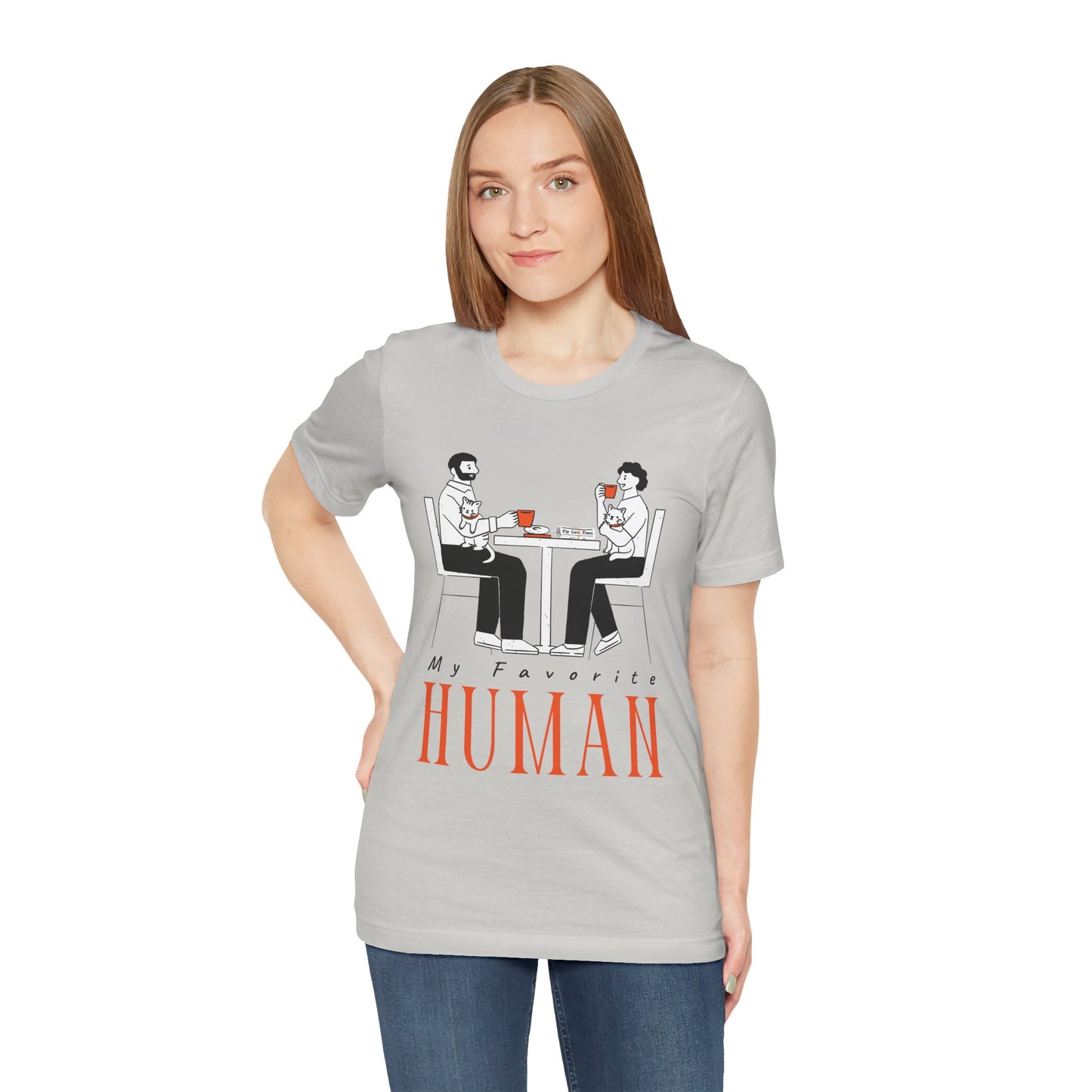 Woman wearing a gray t-shirt with a graphic of two people sitting at a table, newspaper in front of one, drinking hot beverages, holding cats and text 'My Favorite Human' 