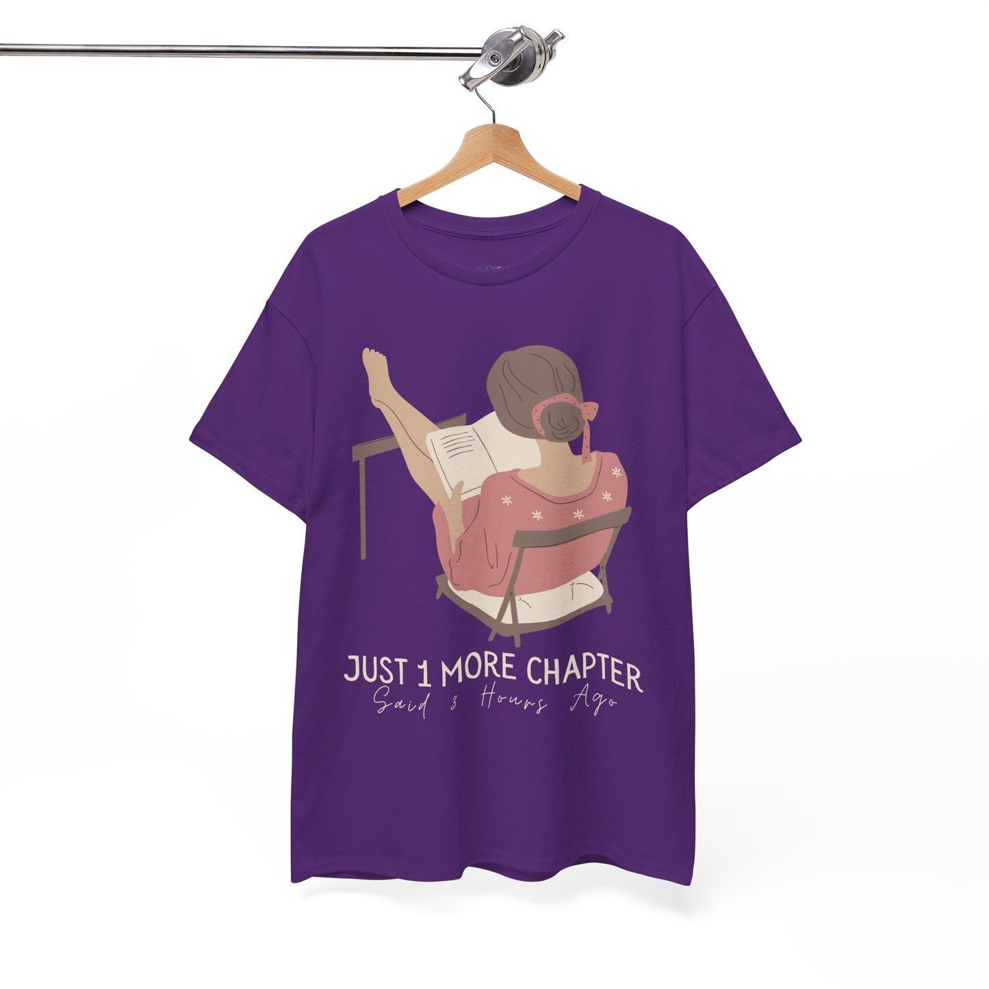 Purple t-shirt with a graphic of a person reading a book with her feet propped up and text 'Just 1 More Chapter, Read's Hours Ago' 
