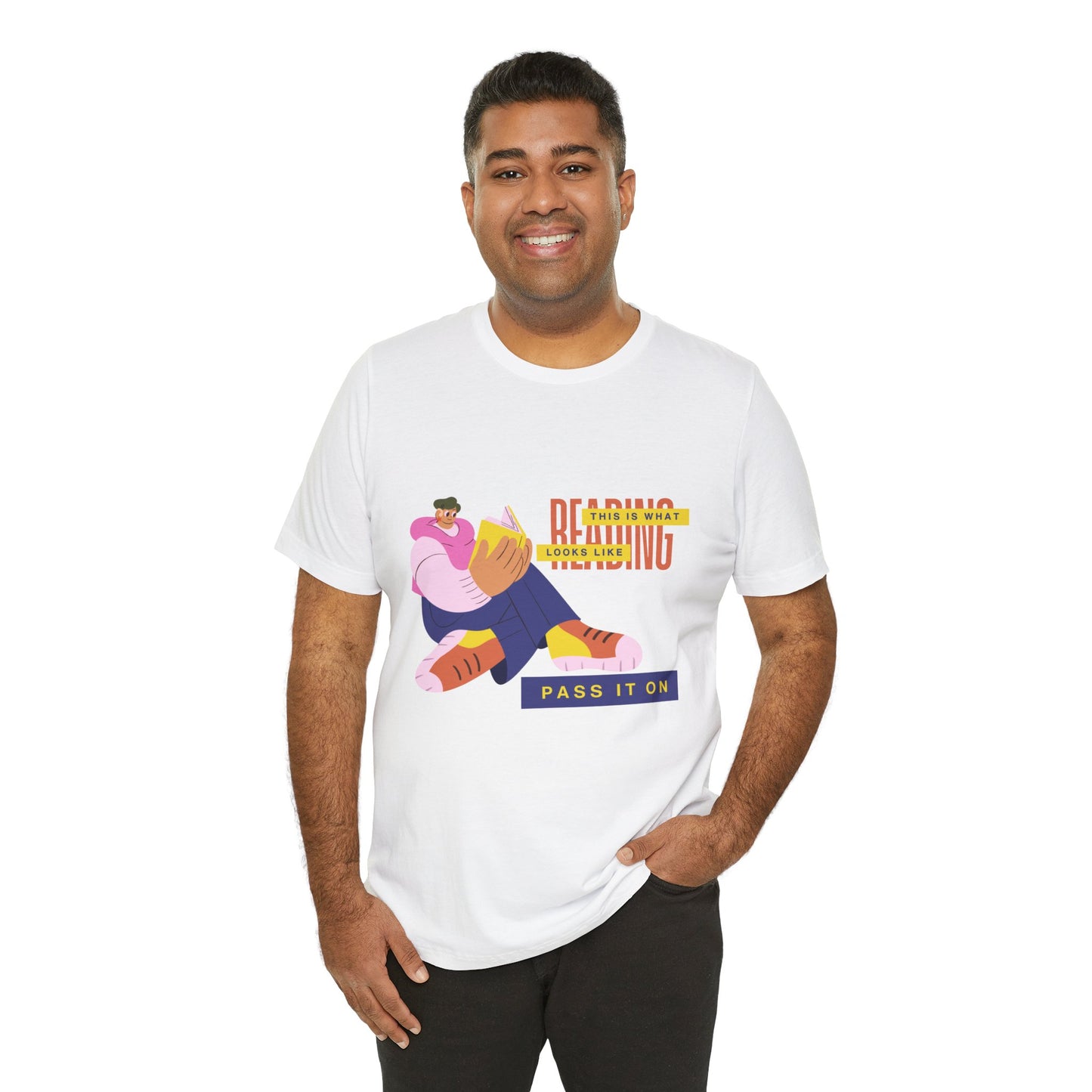Man wearing a white t-shirt with colorful, funny shaped figure reading a book and text 'This Is What Reading Looks Like, Pass It On'