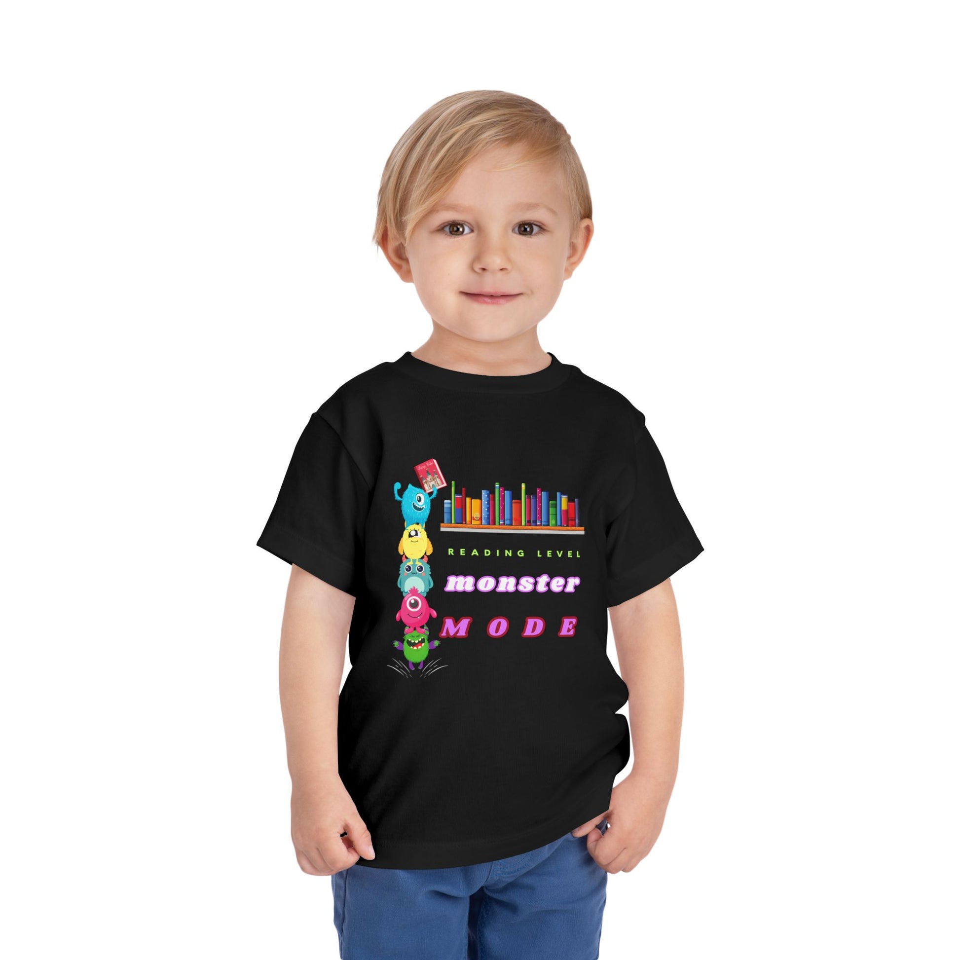 Child wearing a black toddler t-shirt with colorful monsters stacked on top of each other to reach a book from a bookshelf and text 'Reading Level Monster Mode'