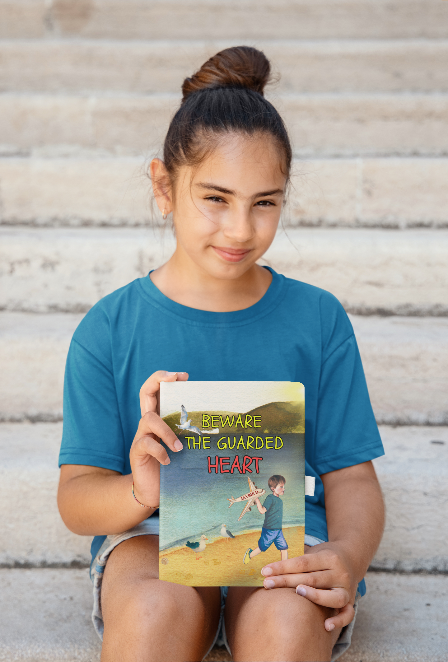 Girl sitting on steps and posing with the children's picture book 'Beware The Guarded Heart' by Jaybie D.