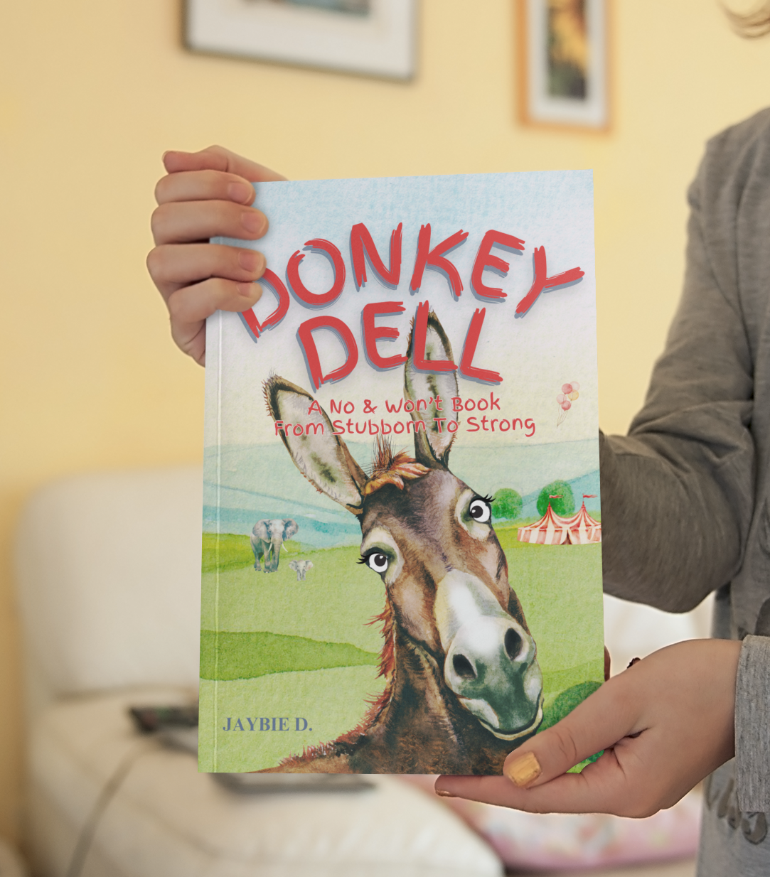 Child holding picture book Donkey Dell by Jaybie D describing a stubborn donkey’s journey toward teamwork, resilience, confidence, and personal growth