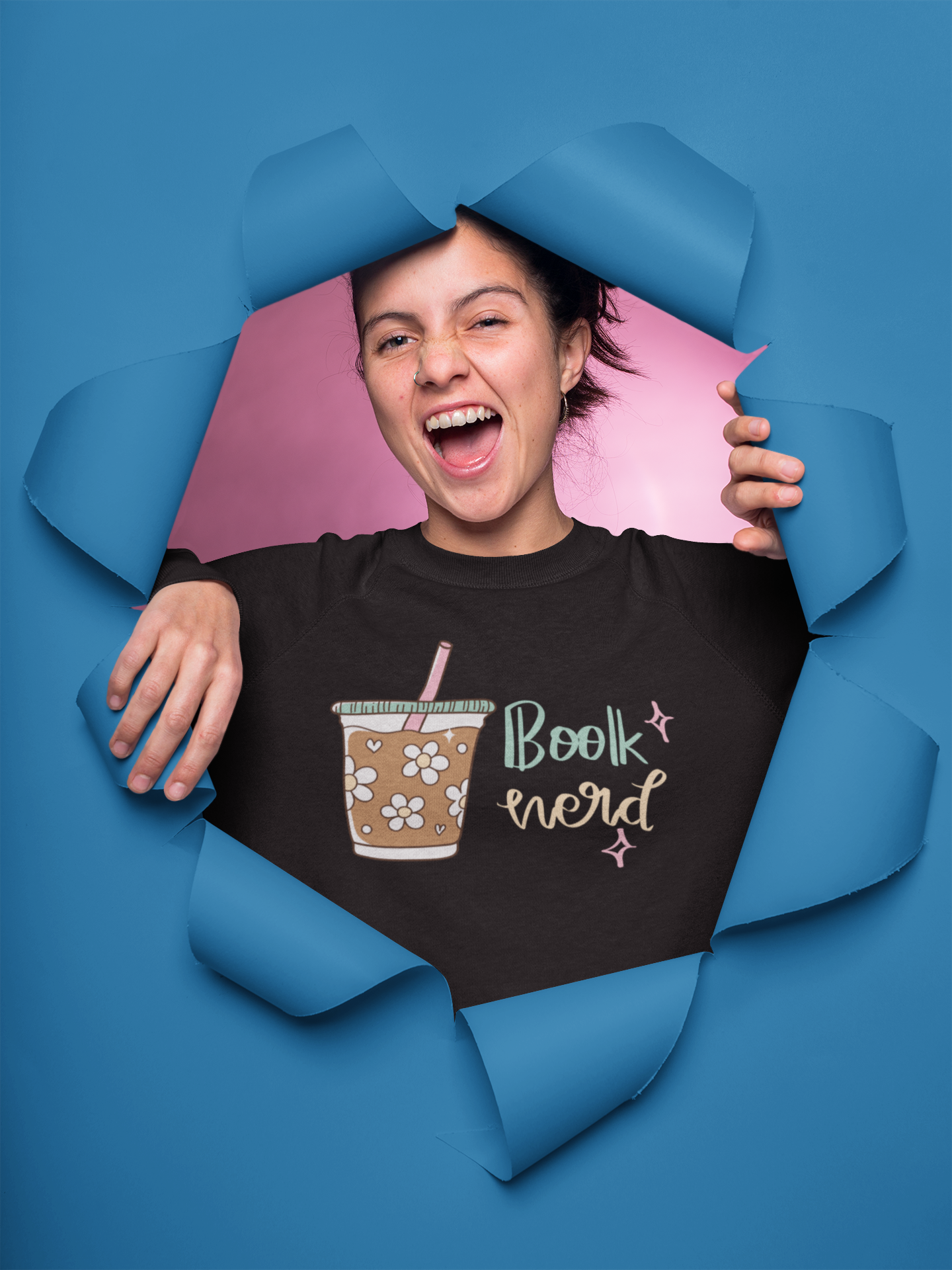 Girl wearing a black t-shirt with a coffee cup and 'Book Nerd' design, peering through torn blue paper.