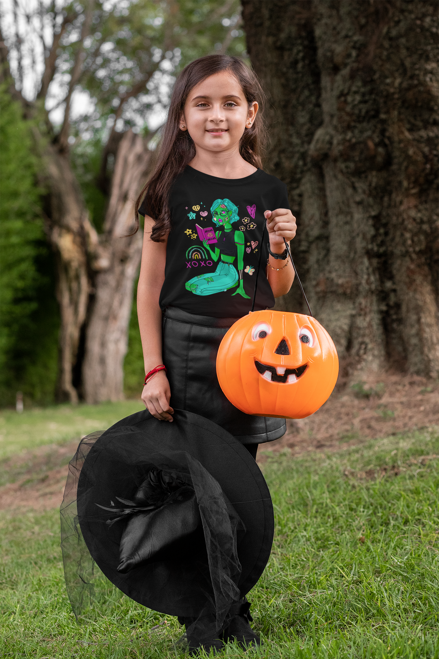 Little girl in a witch costume wearing a green zombie girl shirt.