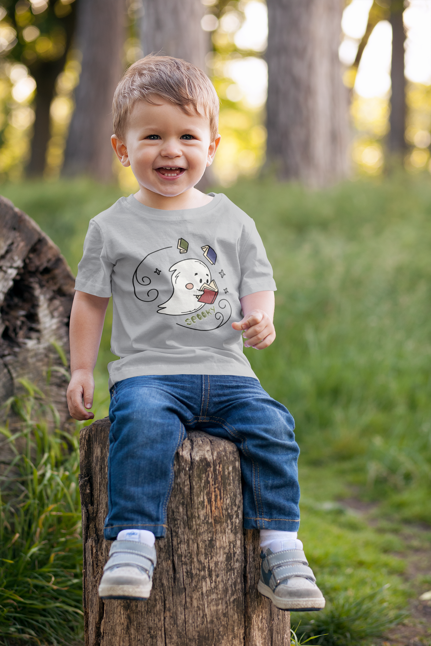 Toddler boy sitting on a tree stump and wearing a gray ghost shirt.